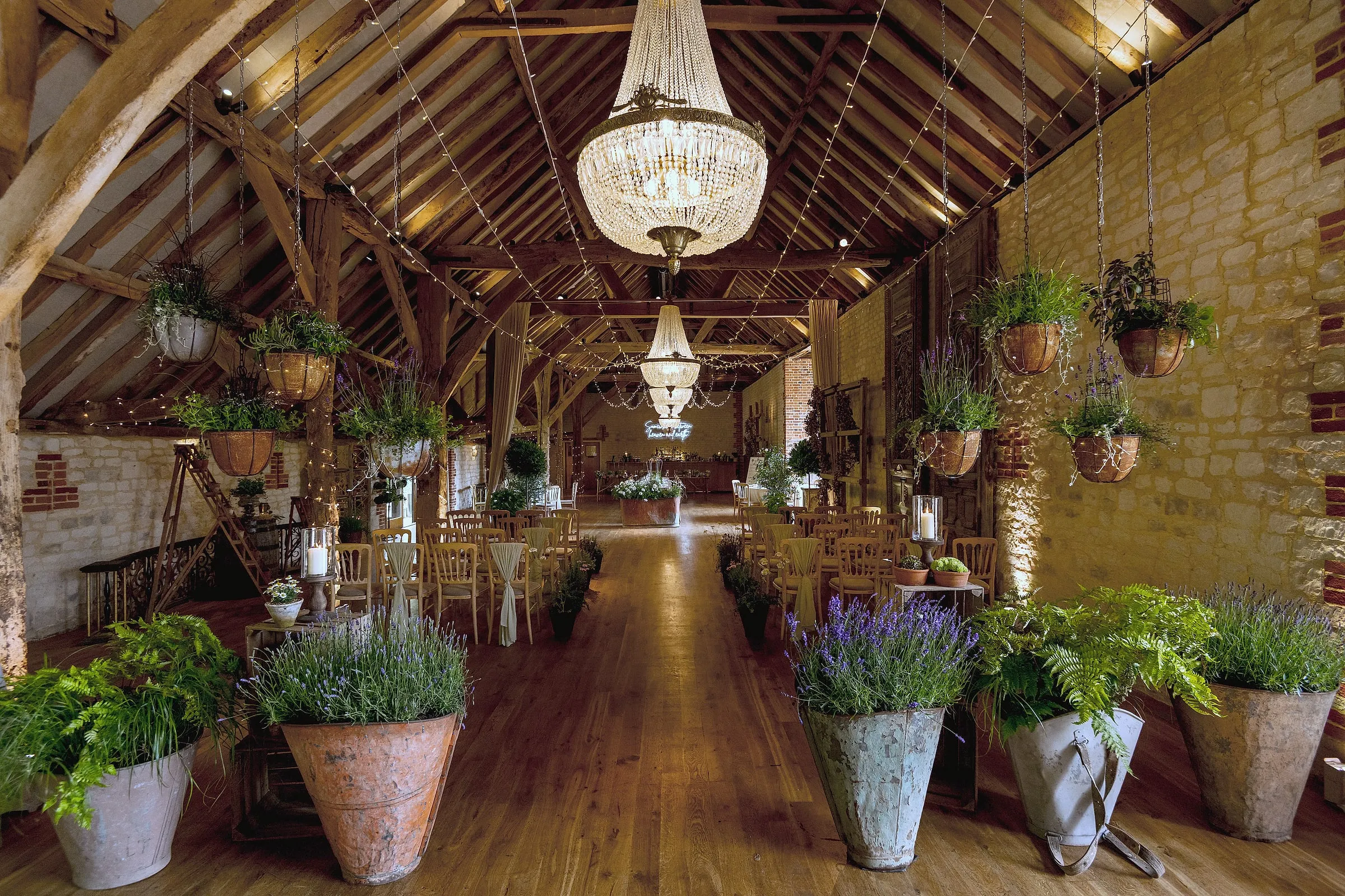 Inside the barn, with chandeliers, oak beams and potted plants along the aisle