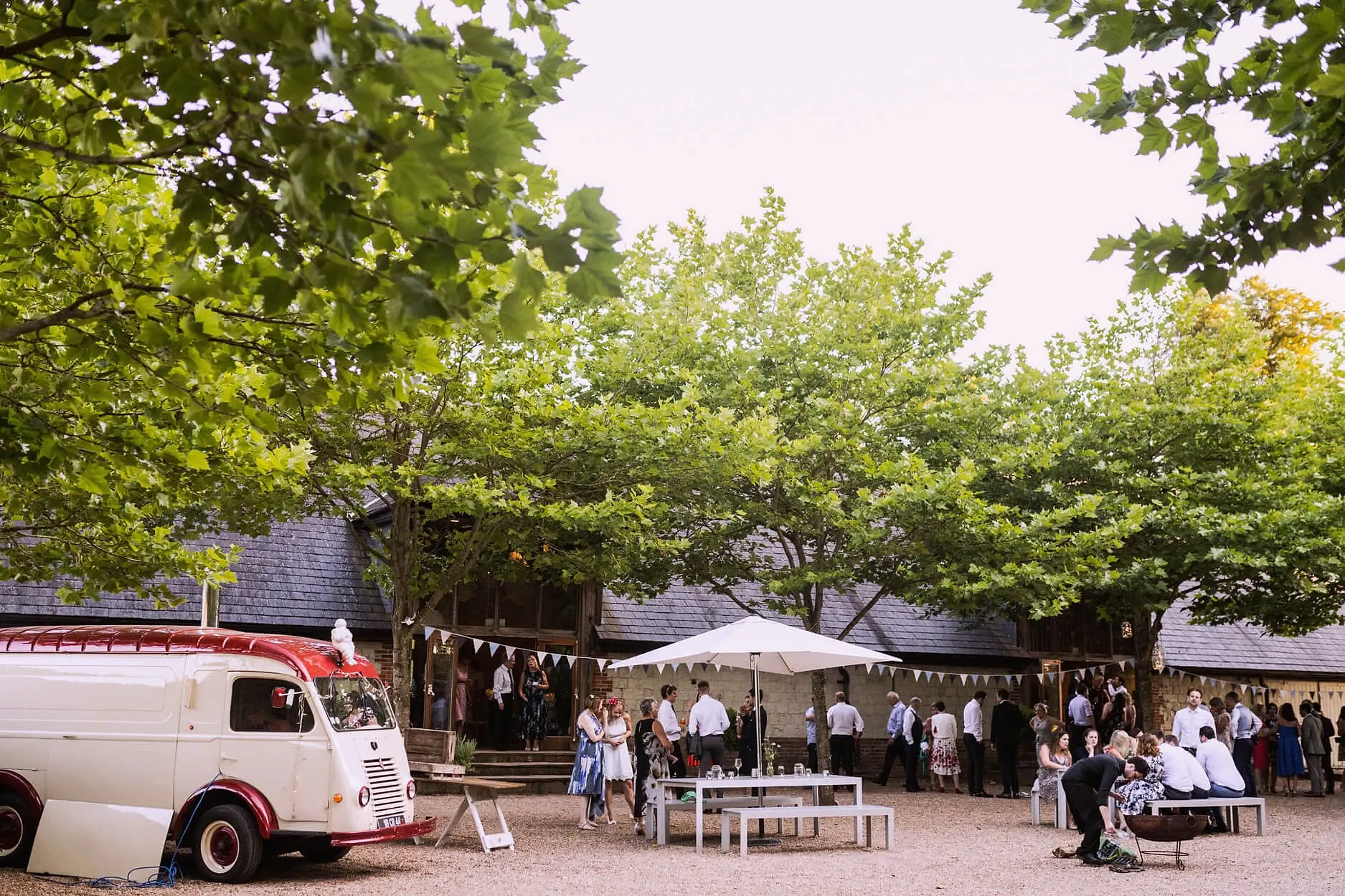 Guests gathered in the courtyard under plane trees and bunting, with a vintage van and parasols