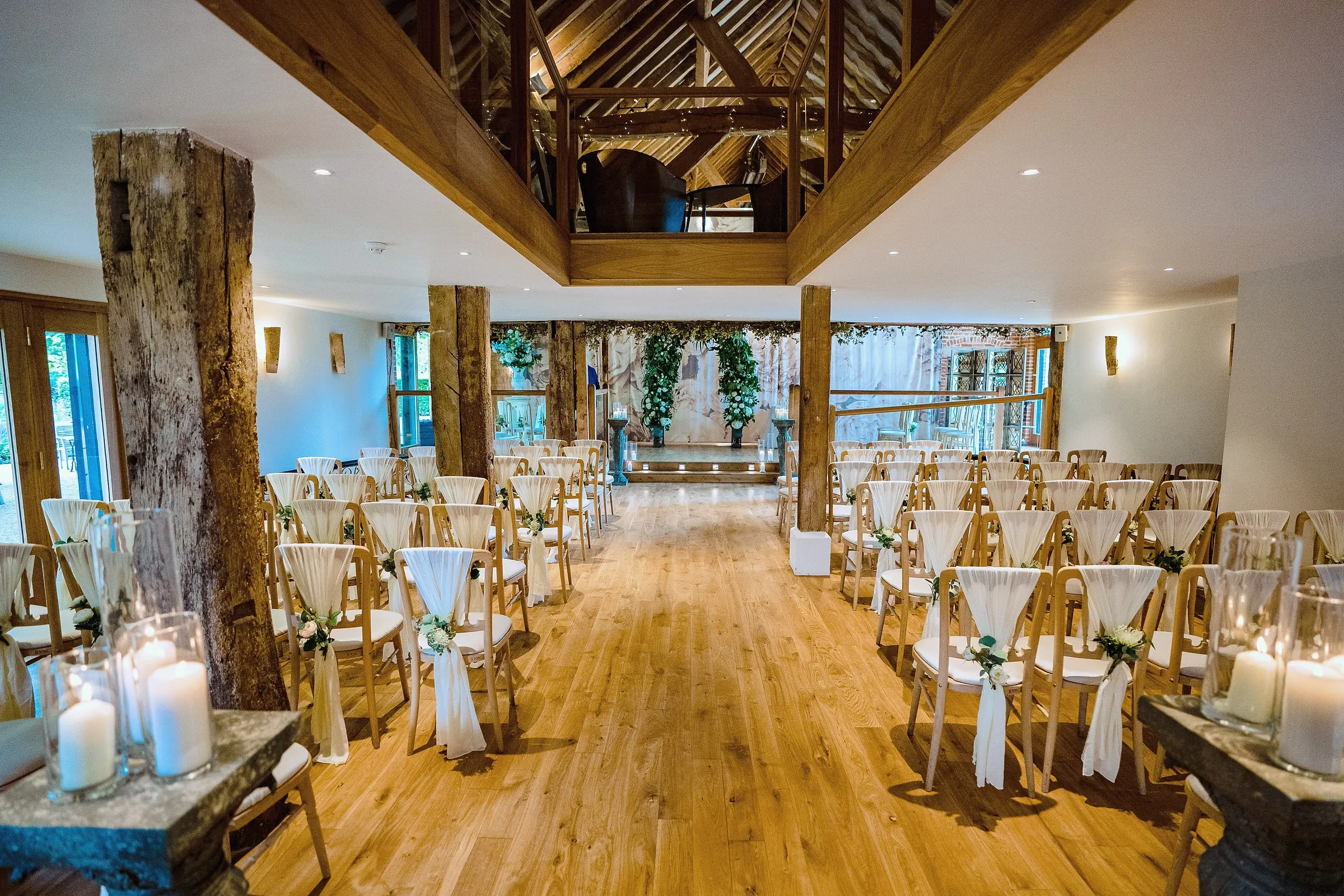 Indoor ceremony room with oak floor, timber posts and chairs dressed with ivory sashes and candles
