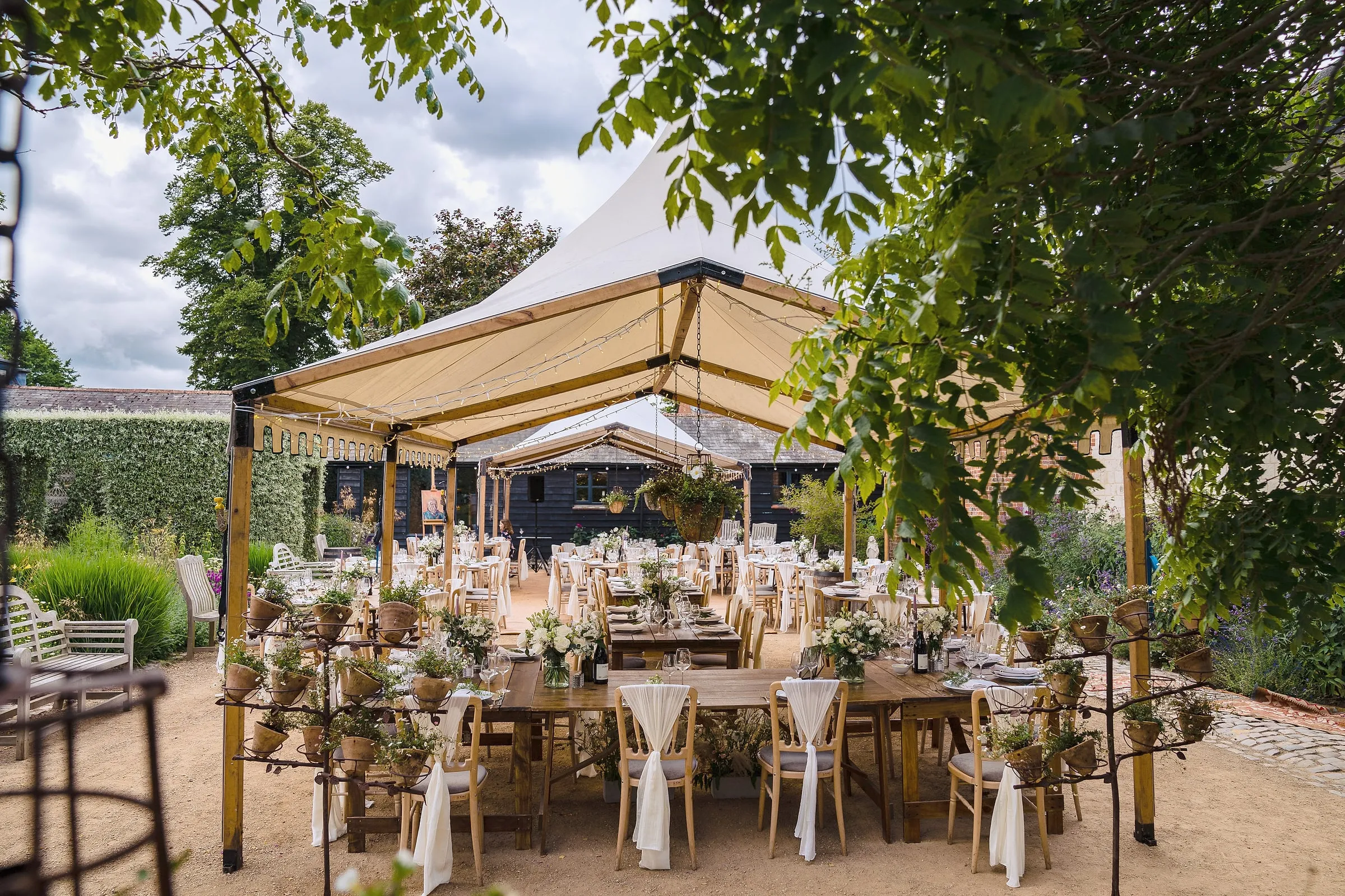 Wooden tables laid under open-sided canopies in the courtyard garden in daylight
