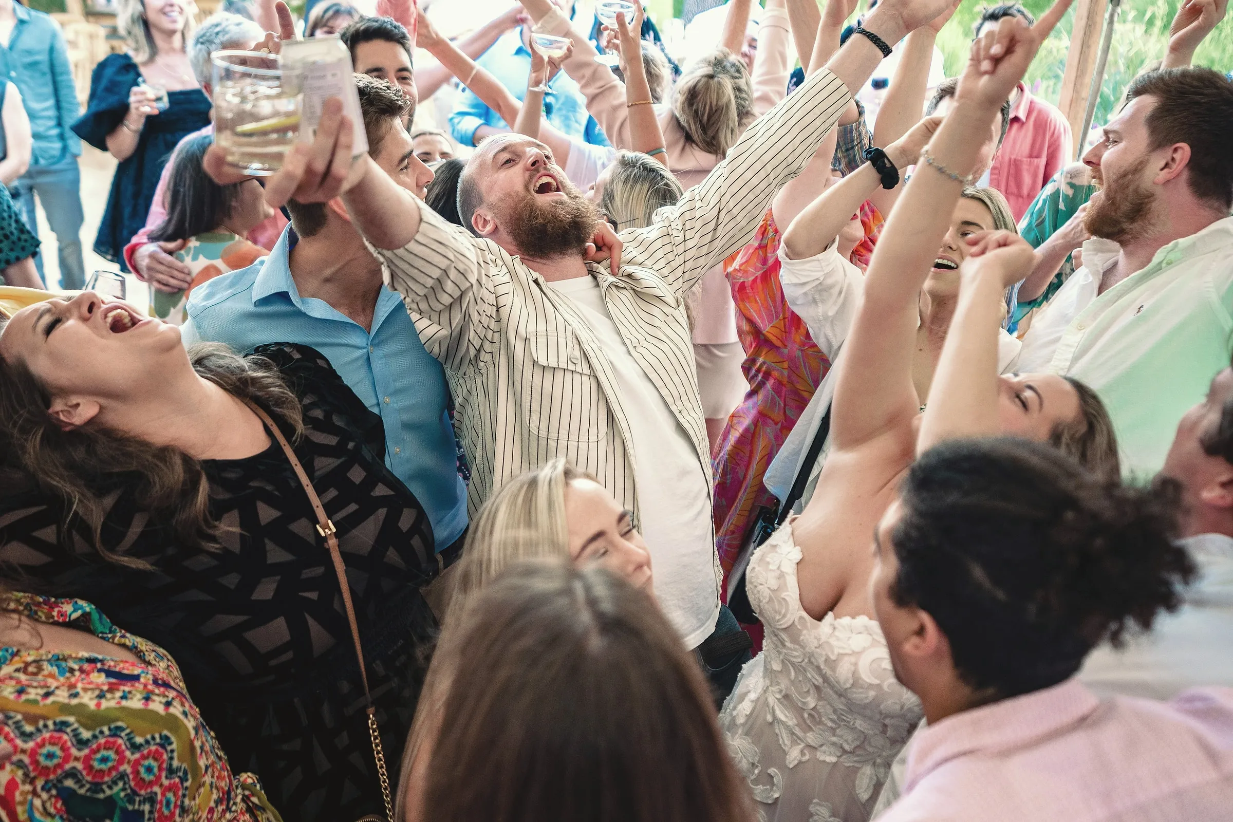 Guests and the bride singing and dancing with raised arms on a packed dance floor