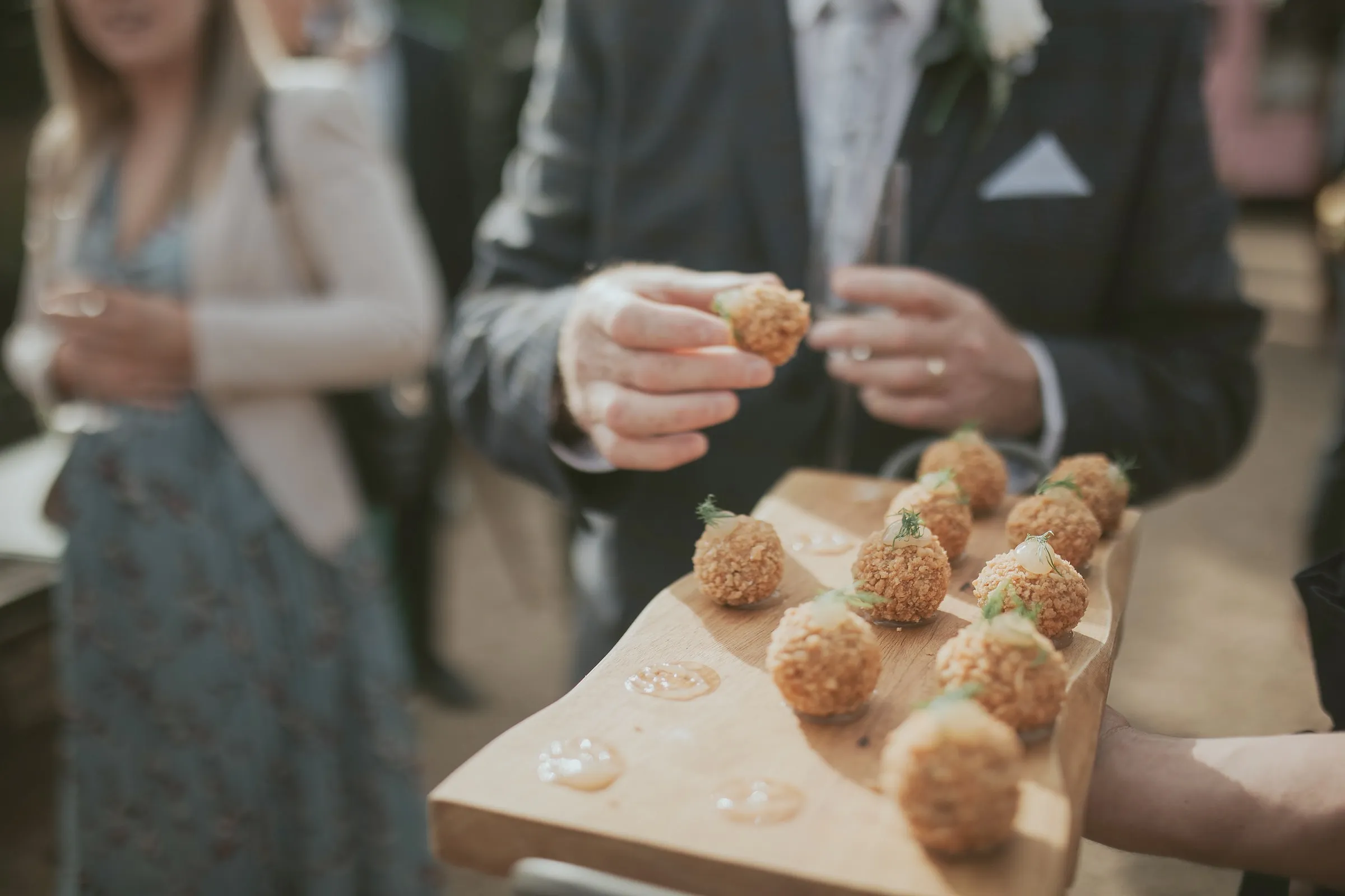 A guest taking an arancini canapé from a wooden serving board
