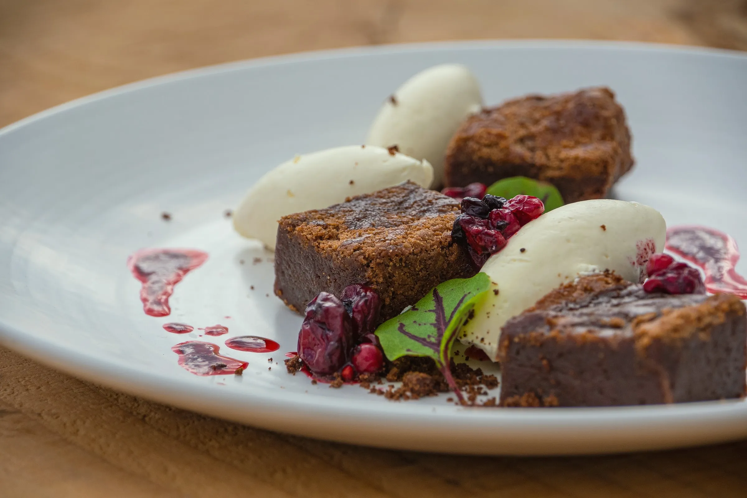 Chocolate brownie squares with quenelles of cream and cherries on a white plate