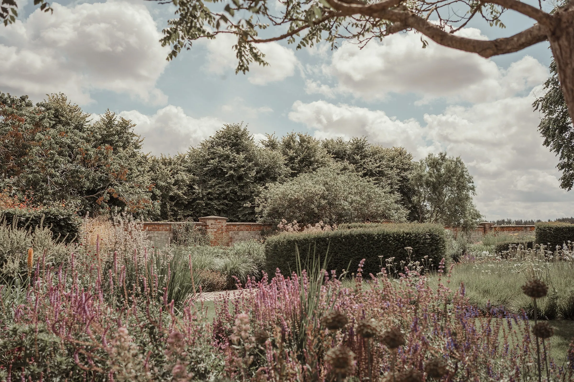 Piet Oudolf's walled garden of pink and purple perennials and clipped yew under a summer sky