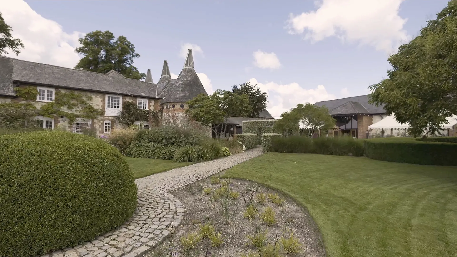 The house, oast roundels and lawn at Bury Court on a bright summer day, from the tour film